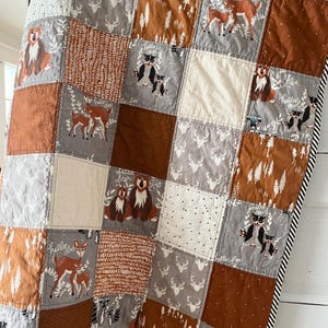 May include: A patchwork quilt with a woodland theme. The quilt features various animals, including deer, owls, bears, and foxes. The quilt is made with a variety of fabrics in shades of brown, grey, and white.