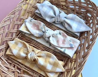 May include: Three fabric headbands in a wicker basket. One headband is blue and white gingham, one is yellow and white gingham, and one is white with a pink floral print.