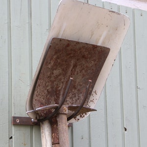 Puede incluir: Una pala de metal oxidada con un mango de metal blanco est&aacute; montada en una pared de madera. La pala est&aacute; colgada boca abajo con el mango apuntando hacia el suelo.