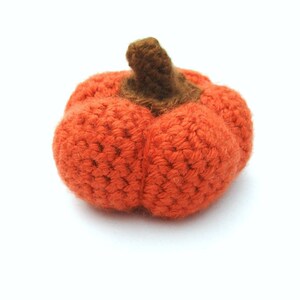 May include: A crocheted orange pumpkin with a brown stem. The pumpkin is made with a textured stitch and has a slightly rounded shape.