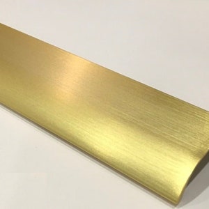 May include: A brushed gold cabinet pull with a rounded edge and a slight curve at the top.