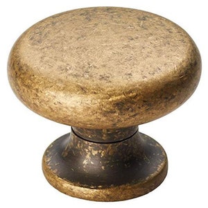 May include: A round, antique brass cabinet knob with a distressed finish. The knob has a raised, rounded top and a smaller, round base.