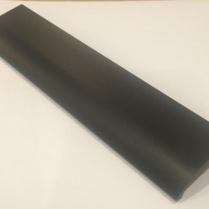 May include: A black metal cabinet pull with a rectangular shape and rounded edges. The pull has a recessed area for gripping.