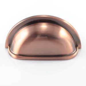 May include: A copper-toned, half-moon cabinet pull. The hardware features a rounded top and a curved, bowl-like design. The finish has a warm, metallic sheen, reflecting light. This drawer pull is a decorative element for furniture.
