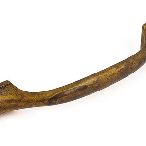 May include: A bronze cabinet pull with a curved handle and rectangular ends. The hardware has a distressed finish, suggesting an antique or vintage style. The pull is designed for easy gripping and opening of drawers or cabinets.