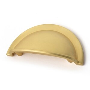 May include: A gold-toned cabinet pull with a rounded, arched shape. The pull is made of metal and has a smooth, polished finish.