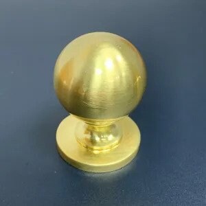 May include: A gold-toned round cabinet knob with a smooth, polished finish. The knob has a raised base and a circular design.