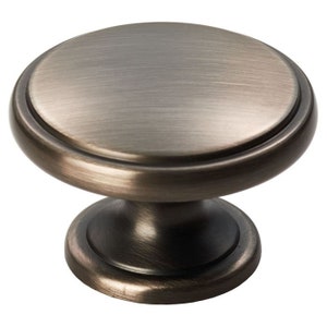 May include: A round, antique brass cabinet knob with a raised, smooth, circular top and a slightly flared base.