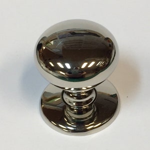 May include: A polished, chrome cabinet knob with a spherical handle. The knob has a circular base and a cylindrical stem connecting the base to the sphere. The reflective surface mirrors the surrounding environment.