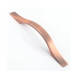 May include: A copper-coloured cabinet handle with a curved design. The handle is smooth and has a brushed finish.