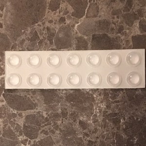 May include: A sheet of white adhesive-backed clear plastic with 16 round, clear, sticky bumpers.