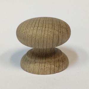 May include: A wooden knob with a rounded top and a slightly raised base. The knob is a light brown colour and has a wood grain pattern.