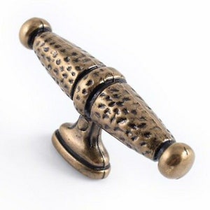May include: A hammered brass cabinet pull with a textured finish. The pull has a rectangular base and a long, curved handle.