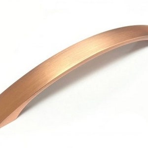 May include: A brushed copper cabinet pull with a curved shape. The pull is approximately 12 inches long.