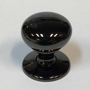 May include: Black cabinet knob with a round, shiny, and slightly domed top. The knob has a round base.