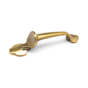 May include: A gold-toned metal cabinet pull with a curved design and a decorative, scalloped edge.