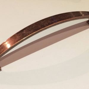 May include: A curved, antique copper cabinet pull with a square base.