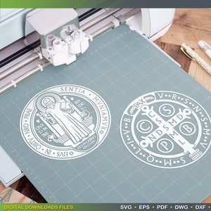 May include: A white outline of the Saint Benedict Medal and the Saint Benedict Cross on a blue background. The Saint Benedict Medal features the image of Saint Benedict holding a book and a cross. The Saint Benedict Cross features the letters "V.R.S.N.S.M.D.P.M.L.I.C.C.S.P.X.A.V.B."