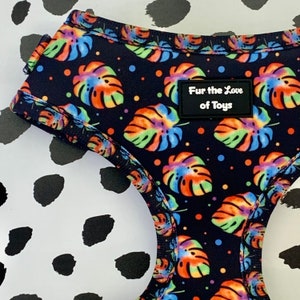 May include: A black dog harness featuring a rainbow tie-dye pattern of monstera leaves and black polka dots. The harness has a black label that reads "Fur the Love of Toys".