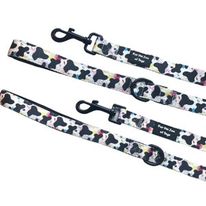 May include: Two black and white dog leads with a colourful splatter pattern. The leads have black metal clips and a black metal ring. The leads are labelled "Fur the Love of Toys".