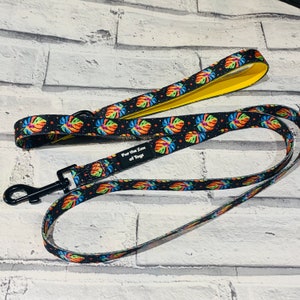 May include: A black dog lead with a colourful tropical leaf pattern and yellow trim. The lead has a black metal clip and a label that reads "Fur the Love of Toys".