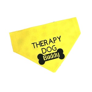 May include: Yellow dog bandana with black text that reads "Therapy Dog Buddy" and a black bone graphic.