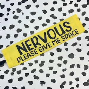 May include: Yellow fabric wristband with black text that reads "NERVOUS PLEASE GIVE ME SPACE".
