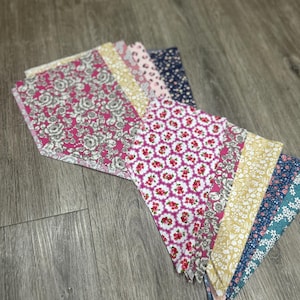 May include: A collection of fabric scraps in various floral patterns, including pink, yellow, blue, and white. The fabric scraps are arranged in a fan shape on a wooden surface.