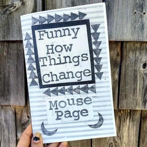 以下が含まれることがあります： 「Funny How Things Change」の文字が黒いフレームで囲まれた本の表紙。その下に「Mouse Page」の文字があります。表紙は、グレーと白のストライプの背景に、黒い矢印と三日月のデザインが施されています。