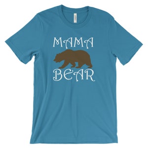 以下が含まれることがあります： ターコイズブルーのTシャツに、白い文字で「ママベア」と書いてあり、茶色のクマのシルエットが描かれています。