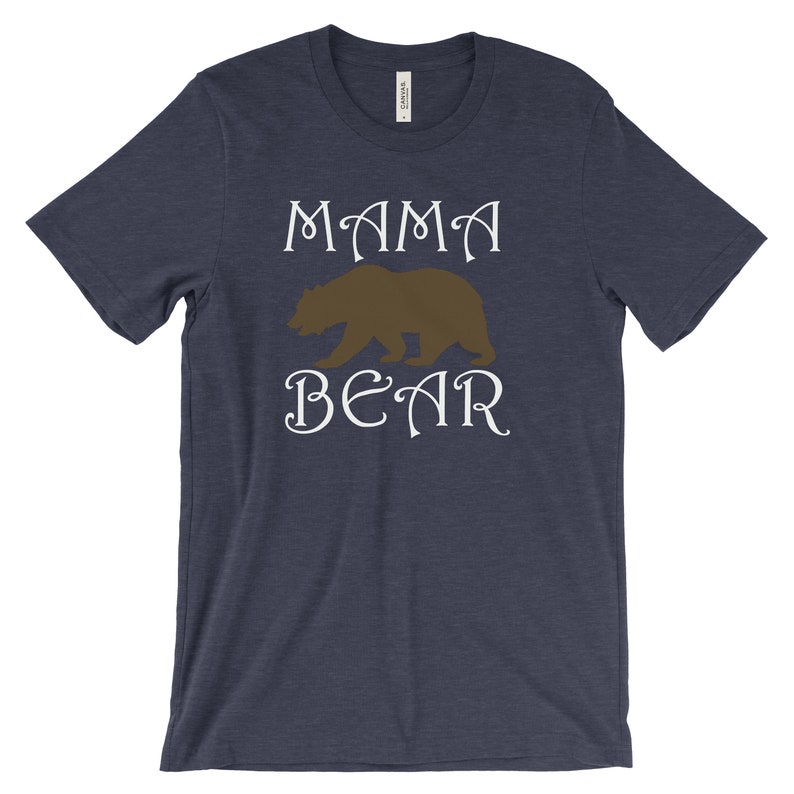以下が含まれることがあります： 白い文字で「ママベア」と書かれたネイビーブルーのTシャツ。茶色の熊のシルエットが単語の間に中央に配置されています。