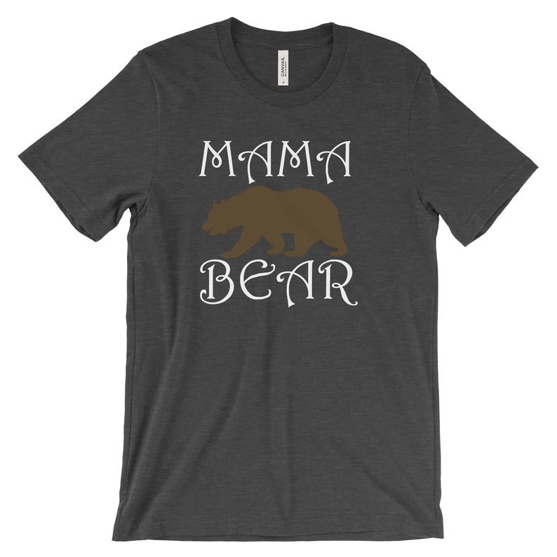 以下が含まれることがあります： 暗いヘザーグレーのTシャツに、白い文字で「ママベア」と書いてあります。文字の間に茶色の熊のシルエットが中央に配置されています。