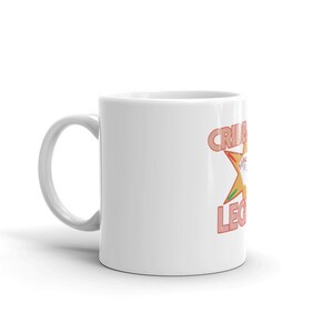 Pode incluir: Caneca de cer&acirc;mica branca com um design rosa e laranja que diz "Criminal Legends" com uma estrela no meio.