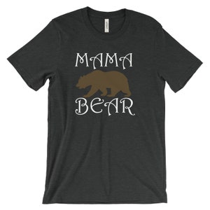 以下が含まれることがあります： 暗いヘザーグレーのTシャツに、白い文字で「MAMA BEAR」と書いてあります。茶色の熊のシルエットが単語の間にあります。