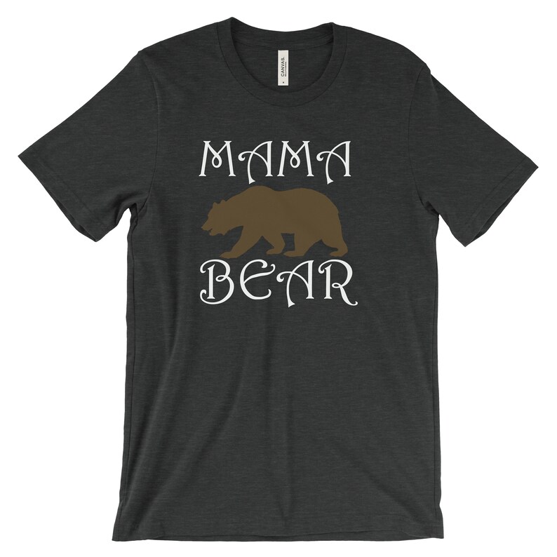 以下が含まれることがあります： 暗いヘザーグレーのTシャツに、白い文字で「MAMA BEAR」と書いてあります。茶色の熊のシルエットが単語の間にあります。
