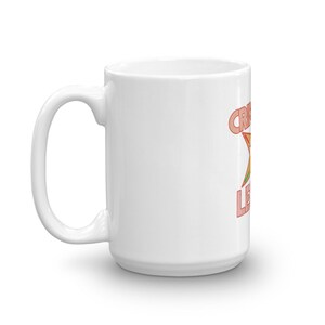Pode incluir: Caneca de cer&acirc;mica branca com um gr&aacute;fico vermelho e laranja de uma estrela e o texto "Crazy Legs" impresso no lado.