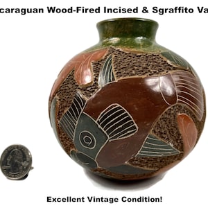 May include: Nicaraguan wood-fired vase with incised and sgraffito design. The vase features a round body with a textured brown surface, accented with leaf-like shapes in shades of brown, green, and gray. The rim is green, and the vase is in excellent vintage condition.