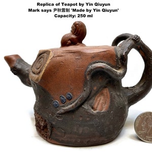 May include: A replica teapot by Yin Qiuyun, with a capacity of 250 ml. The teapot is brown and black with a unique, textured design. The lid features a small sculpture. The text on the image says "Made by Yin Qiuyun".