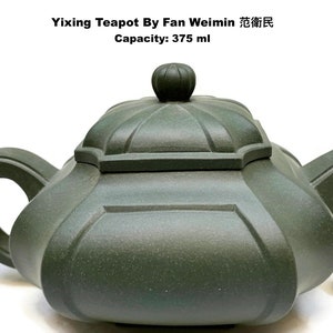May include: A dark green Yixing teapot by Fan Weimin with a capacity of 375 ml. The teapot has a unique, geometric design with a rounded handle and a lid with a small knob. A quarter is next to the teapot for size comparison.
