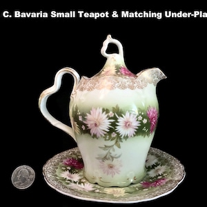 May include: A small R. C. Bavaria teapot and matching under-plate. The teapot and plate are decorated with pink and white flowers and gold trim. The teapot has a heart-shaped handle. The text "R. C. Bavaria Small Teapot & Matching Under-Plate" is at the top.