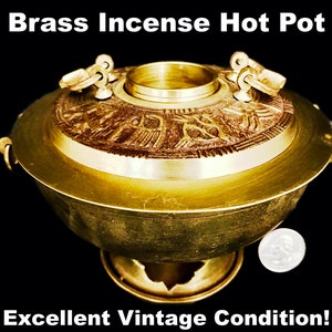 May include: A brass incense hot pot with a round base and a lid. The lid features ornate carvings and two handles. The pot is gold-colored and has a vintage appearance. The text "Brass Incense Hot Pot" and "Excellent Vintage Condition!" are visible.
