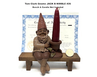 Könnte beinhalten: Eine Tom Clark Zwergenfigur mit dem Titel Jack B Nimble #26, bestehend aus einem braunen, strukturierten Zwerg mit spitzem Hut und Bart, der neben einem Kerzenhalter sitzt. Der Text lautet Tom Clark Gnome JACK B NIMBLE #26 Bench & Candle Not Included.