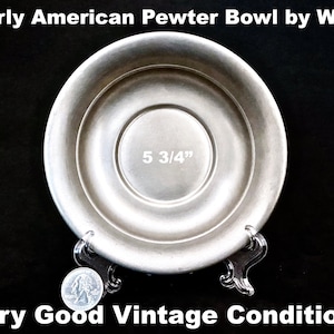 May include: Early American pewter bowl, 5 3/4 inches in diameter, with a circular design. The bowl is displayed on a clear stand. The text "Early American Pewter Bowl by WEB" and "Very Good Vintage Condition!" are visible.