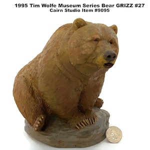 May include: A brown bear figurine from the 1995 Tim Wolfe Museum Series, Grizz #27, by Cairn Studio. The bear is seated on a rock base, with detailed fur texture and a realistic expression. The figurine is a collectible item.