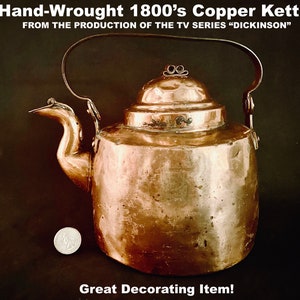 May include: A hand-wrought copper kettle from the 1800s, with a curved spout and handle. The text on the image reads "Hand-Wrought 1800's Copper Kettle FROM THE PRODUCTION OF THE TV SERIES 'DICKINSON' Great Decorating Item!"