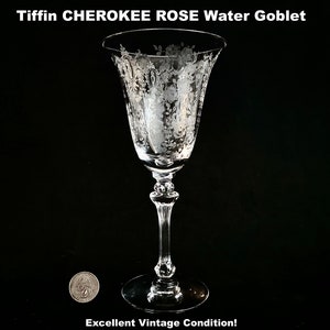 May include: Clear Tiffin Cherokee Rose water goblet with etched floral design. The glass has a long stem and a wide, flared bowl. The text "Tiffin CHEROKEE ROSE Water Goblet" is at the top. The text "Excellent Vintage Condition!" is at the bottom.