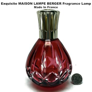 May include: A deep red glass fragrance lamp with a faceted diamond-like pattern and a silver-toned metal crown top. The text Exquisite MAISON LAMPE BERGER Fragrance Lamp Made In France is visible above. A US quarter coin is placed next to the base.