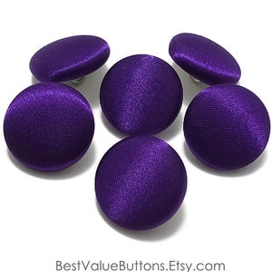 May include: Six purple satin buttons with silver shanks. The buttons are round and have a smooth, shiny finish.
