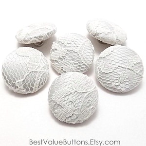 May include: Six white lace buttons with a delicate floral pattern. The buttons are round and have a smooth, satin-like finish.