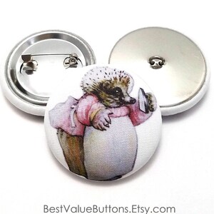 May include: A white button with a colorful illustration of a hedgehog wearing a pink dress and holding a mirror. The button has a metal pin back.
